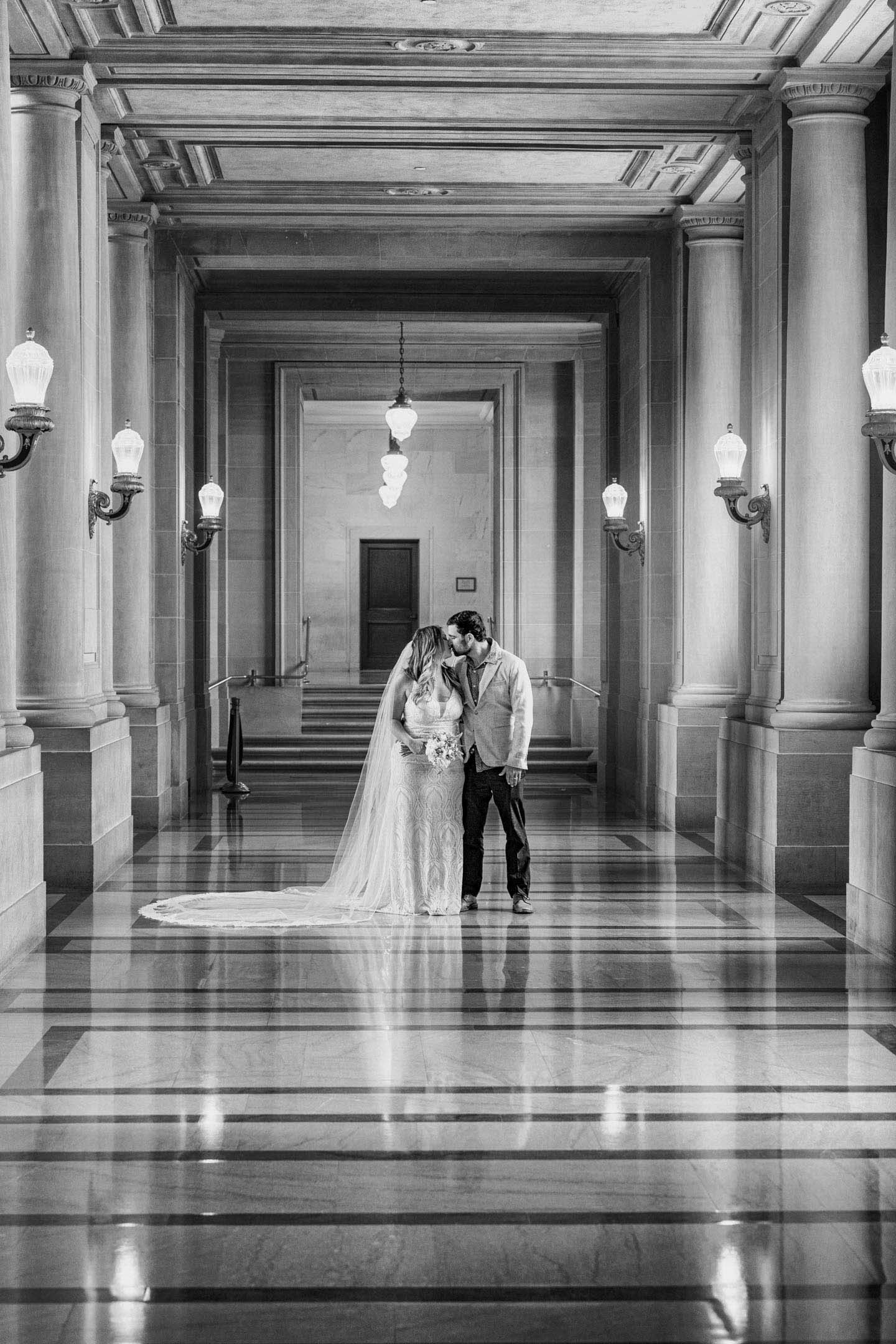 Bride and groom kiss in a grand marble hall, black and white